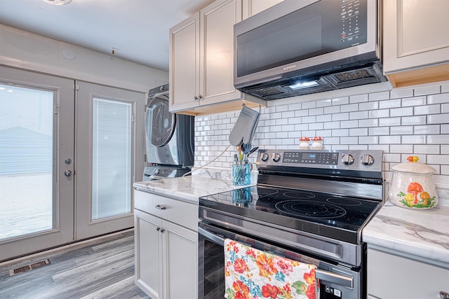 kitchen featuring visible vents, stacked washer / drying machine, light stone countertops, french doors, and stainless steel range with electric stovetop