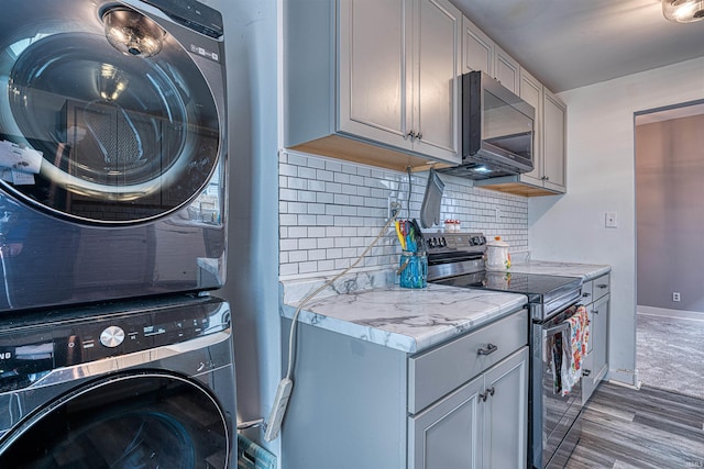 laundry area featuring laundry area, baseboards, stacked washer / drying machine, and wood finished floors