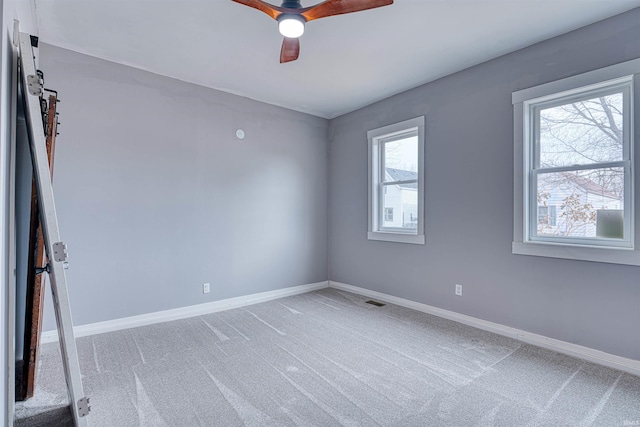 carpeted spare room featuring a barn door, baseboards, and ceiling fan