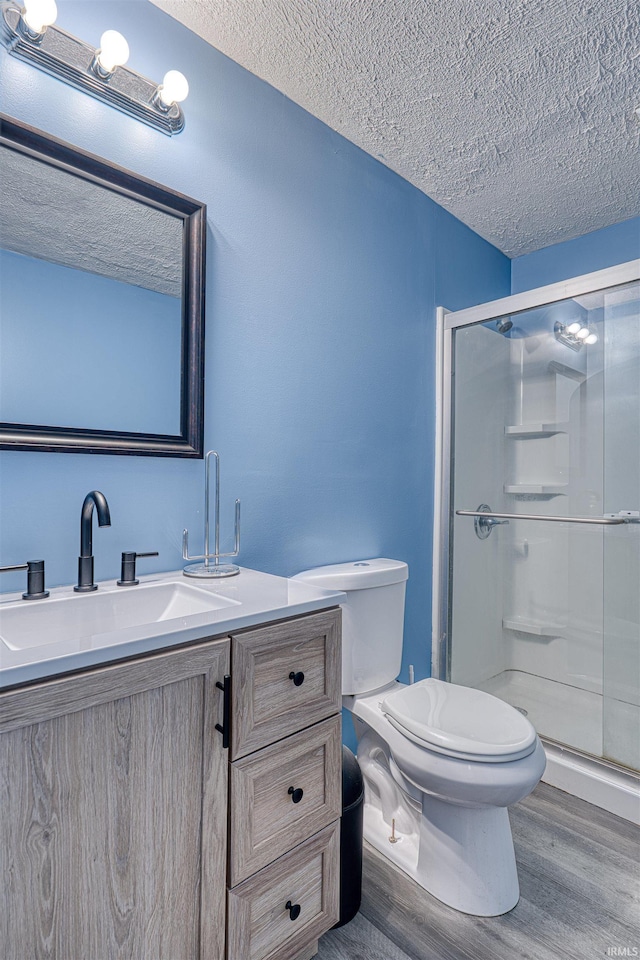 bathroom with a textured ceiling, wood finished floors, toilet, and a shower stall