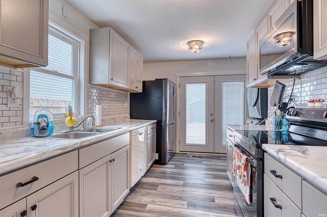 kitchen featuring light wood finished floors, tasteful backsplash, appliances with stainless steel finishes, light stone counters, and white cabinetry