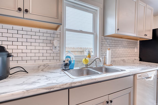 kitchen with tasteful backsplash, light stone counters, white dishwasher, white cabinetry, and a sink