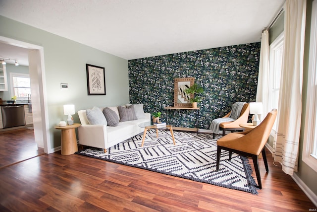 living area with wallpapered walls, an accent wall, baseboards, and wood finished floors