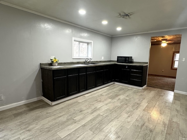 kitchen featuring light wood-style flooring, light countertops, crown molding, black microwave, and a sink