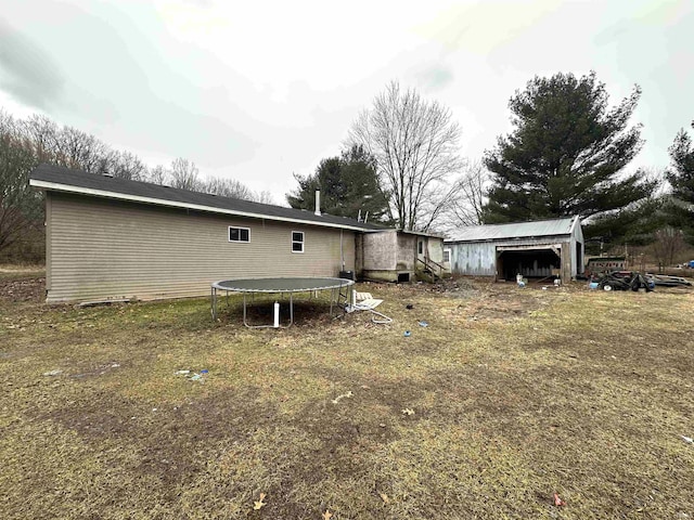 rear view of property with an outbuilding, a trampoline, and a lawn