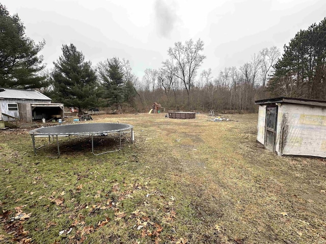 view of yard featuring a shed, a trampoline, and an outbuilding