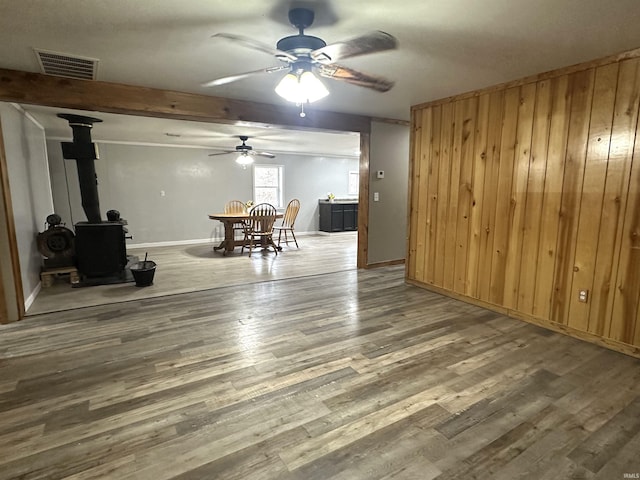 unfurnished living room with visible vents, a wood stove, ceiling fan, wood finished floors, and baseboards