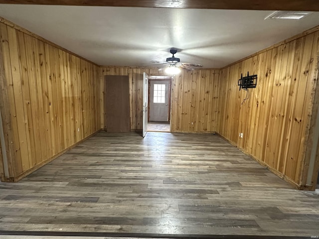 empty room featuring wood walls, visible vents, a ceiling fan, and wood finished floors