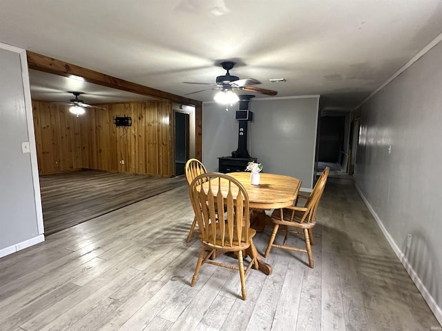 dining space with wood-type flooring, visible vents, a ceiling fan, a wood stove, and baseboards