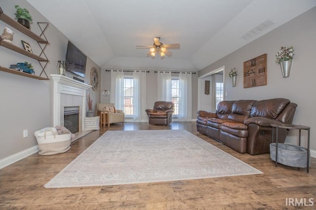 living area featuring ceiling fan, a tile fireplace, wood finished floors, visible vents, and baseboards