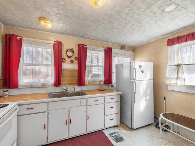 kitchen with tile countertops, white appliances, white cabinetry, and a sink