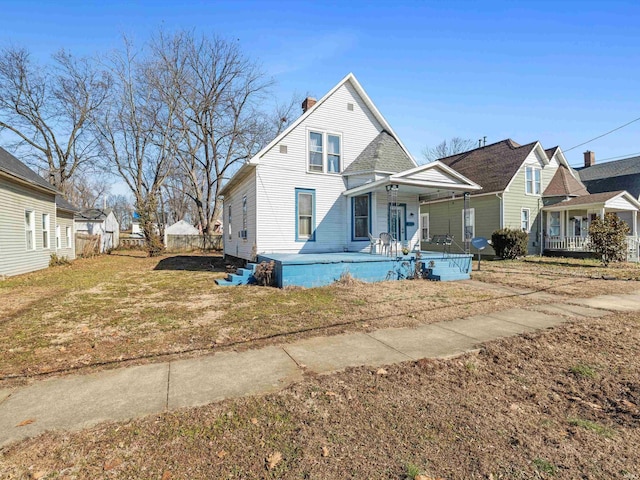 view of front of property featuring covered porch, a chimney, fence, and a front yard