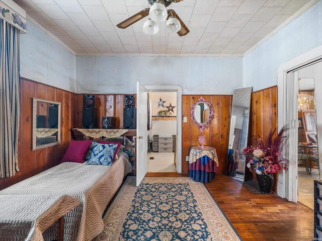 bedroom featuring crown molding, wooden walls, a ceiling fan, and wood finished floors