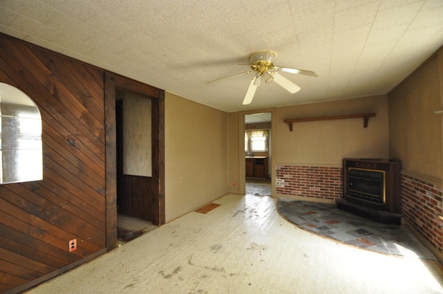 unfurnished living room with ceiling fan, carpet floors, wood walls, and arched walkways