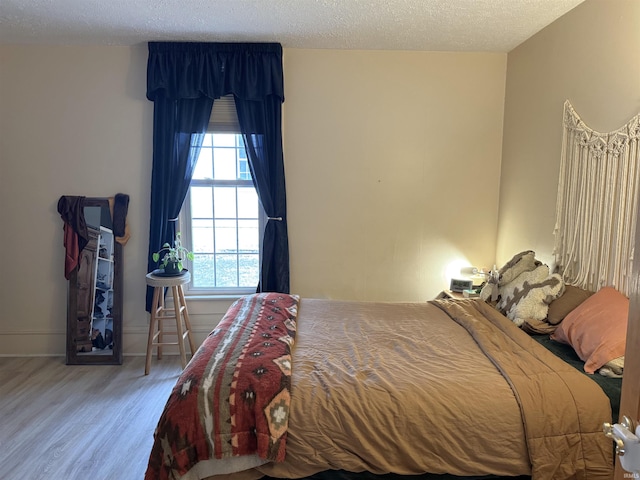 bedroom with a textured ceiling, baseboards, and wood finished floors