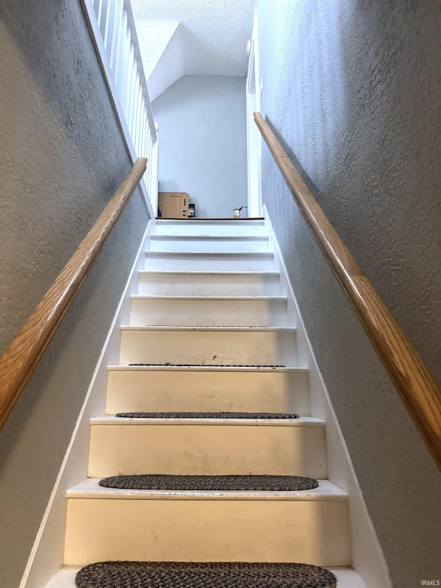 staircase featuring lofted ceiling and a textured wall