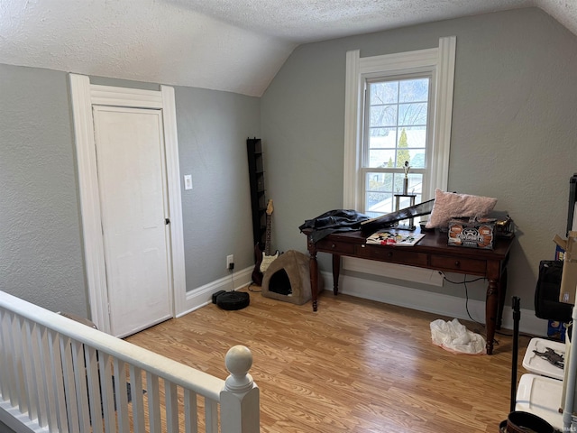 workout room with a textured ceiling, vaulted ceiling, baseboards, and light wood-style floors