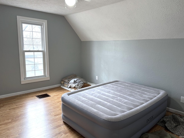 bedroom featuring lofted ceiling, multiple windows, wood finished floors, and visible vents