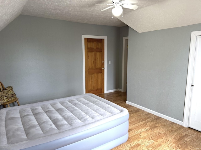 bedroom with a textured ceiling, baseboards, vaulted ceiling, and wood finished floors