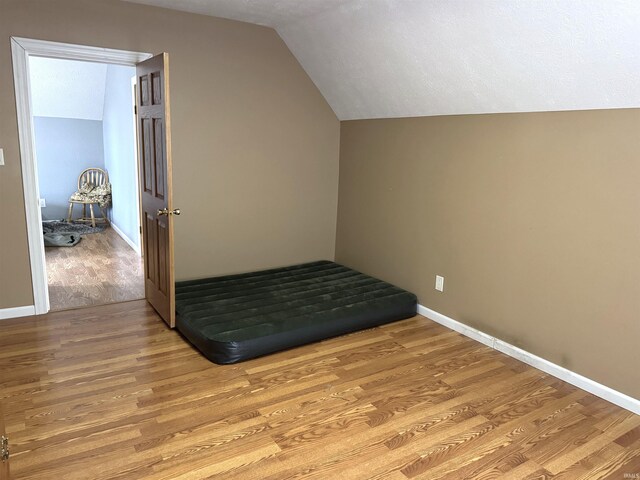 unfurnished bedroom featuring lofted ceiling, light wood-style flooring, and baseboards