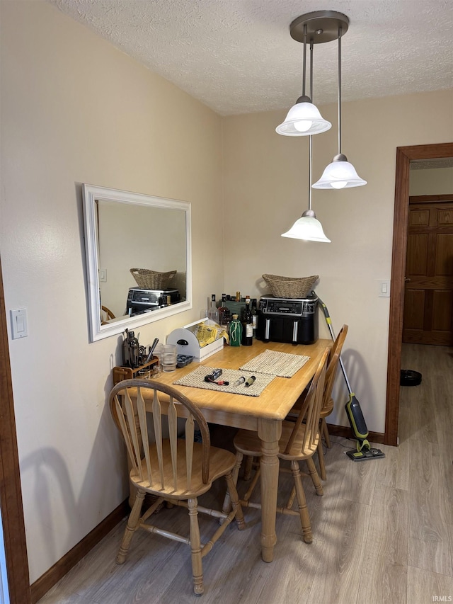 dining space featuring a textured ceiling, wood finished floors, and baseboards