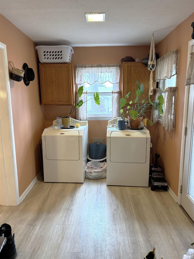 washroom featuring cabinet space, light wood finished floors, baseboards, washing machine and clothes dryer, and a textured ceiling