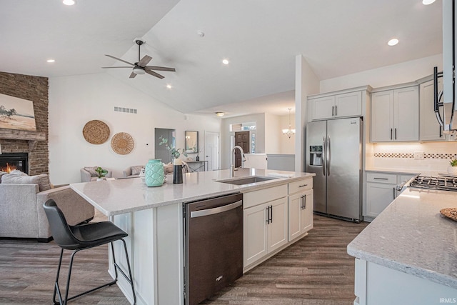 kitchen featuring a fireplace, a center island with sink, stainless steel appliances, open floor plan, and a sink