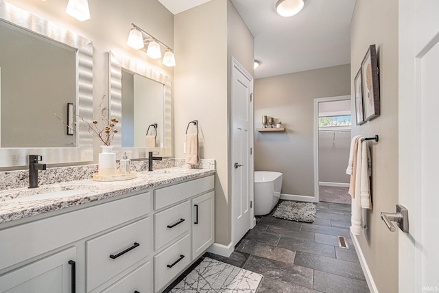 full bath with a sink, stone tile flooring, and baseboards