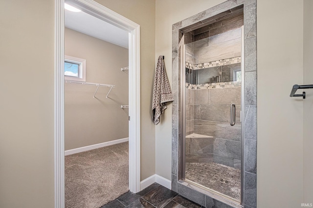 bathroom featuring a shower stall, a spacious closet, and baseboards