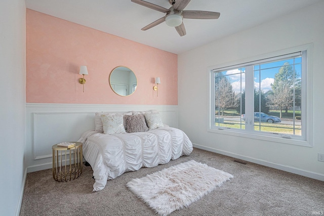 bedroom with a ceiling fan, carpet, a wainscoted wall, and visible vents