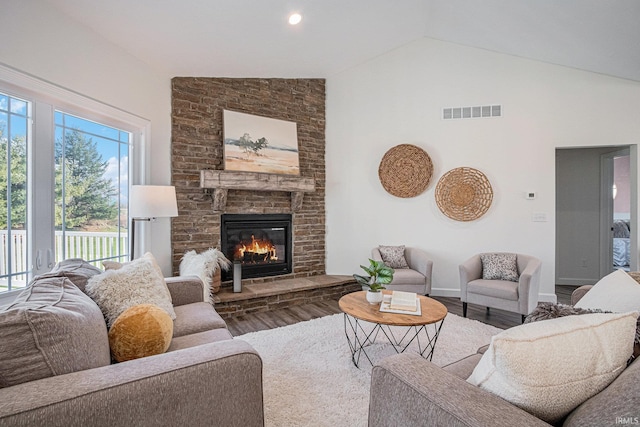 living area with a large fireplace, baseboards, visible vents, wood finished floors, and high vaulted ceiling