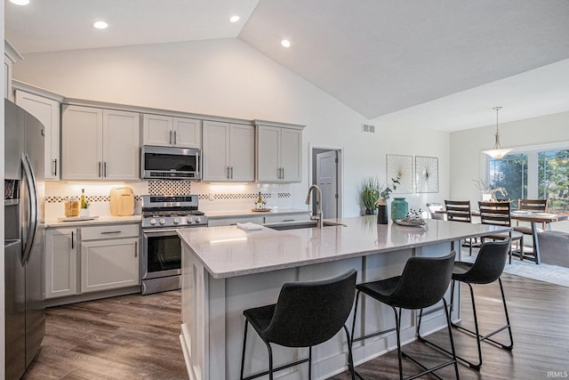 kitchen with stainless steel appliances, a sink, visible vents, a kitchen breakfast bar, and dark wood-style floors