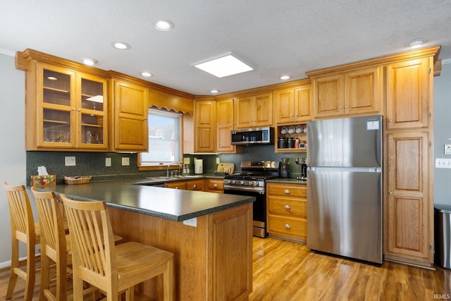 kitchen featuring brown cabinets, stainless steel appliances, dark countertops, a sink, and a peninsula