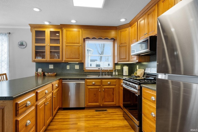 kitchen with dark countertops, appliances with stainless steel finishes, brown cabinetry, and a sink