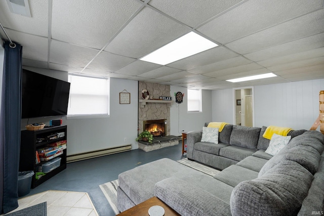 living room with finished concrete flooring, a baseboard radiator, a drop ceiling, and a stone fireplace