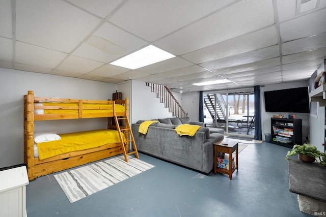 living room with concrete flooring, a drop ceiling, and stairway