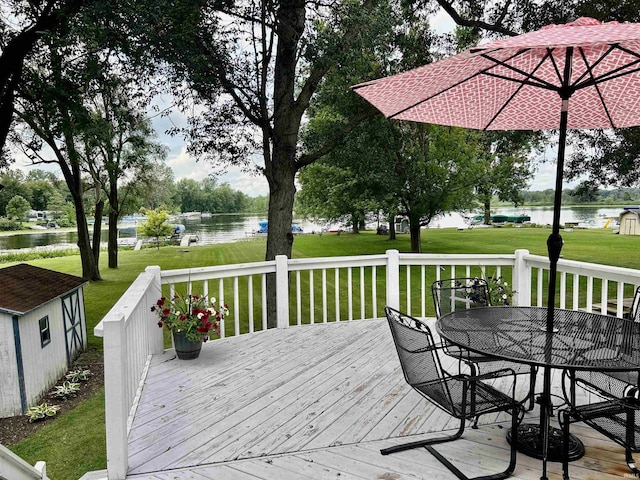 wooden deck with a yard, outdoor dining space, a water view, and an outdoor structure