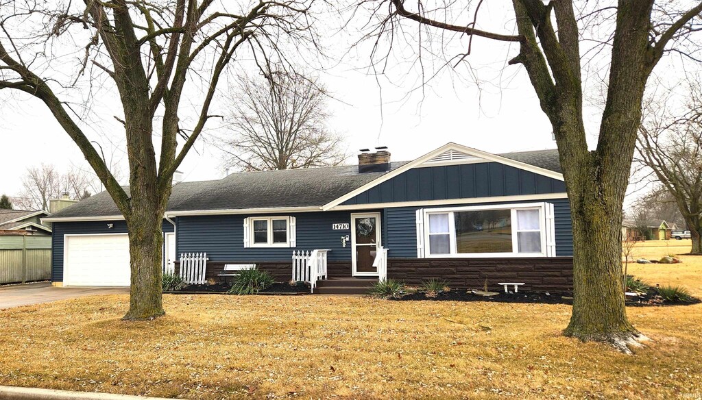 view of front of house featuring an attached garage, a shingled roof, driveway, board and batten siding, and a chimney