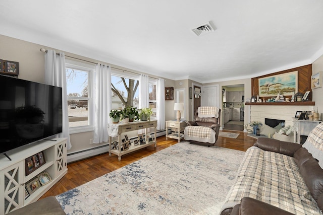 living area with a fireplace with flush hearth, a baseboard heating unit, wood finished floors, and visible vents