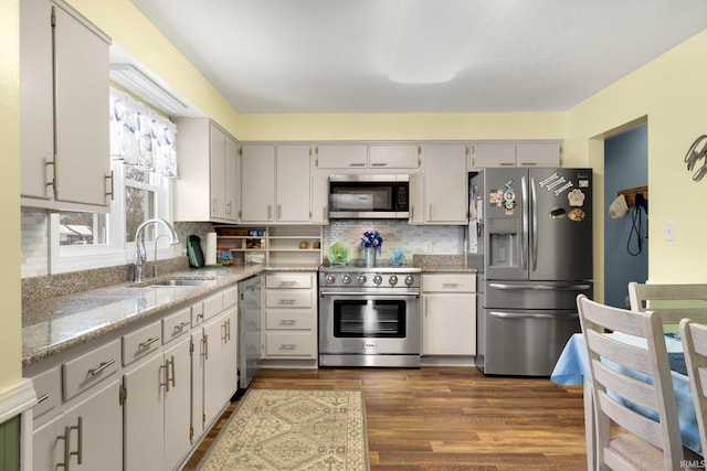 kitchen featuring a sink, appliances with stainless steel finishes, backsplash, light stone countertops, and dark wood finished floors