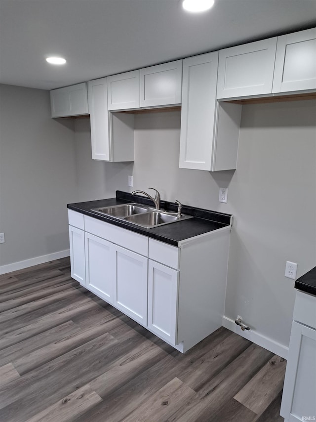 kitchen with dark wood-style floors, dark countertops, a sink, and white cabinetry