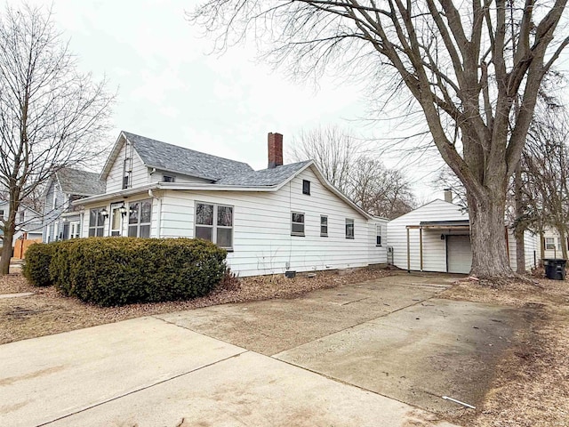 view of side of home with an outbuilding, a shingled roof, a chimney, and a garage