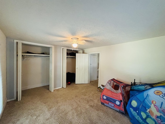 bedroom with multiple closets, light carpet, a textured ceiling, and a ceiling fan