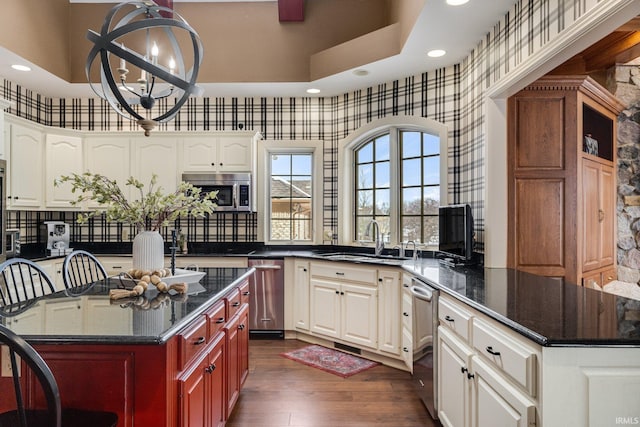 kitchen featuring stainless steel appliances, a kitchen island, a sink, dark wood finished floors, and wallpapered walls