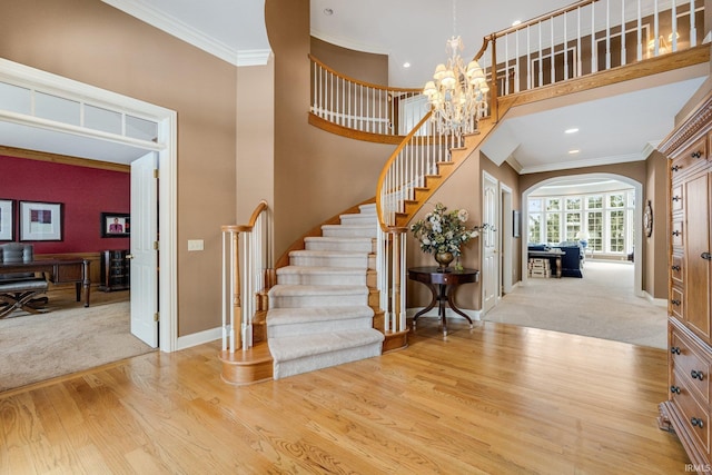 carpeted entryway featuring stairway, arched walkways, crown molding, and wood finished floors