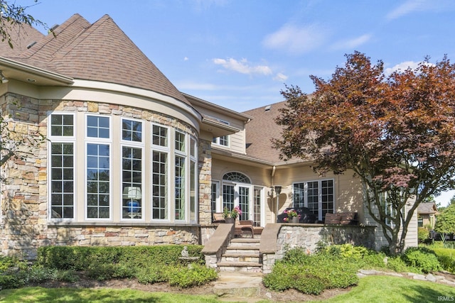 view of exterior entry featuring stone siding, a shingled roof, and french doors