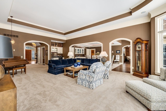 living area featuring visible vents, arched walkways, carpet flooring, and ornamental molding