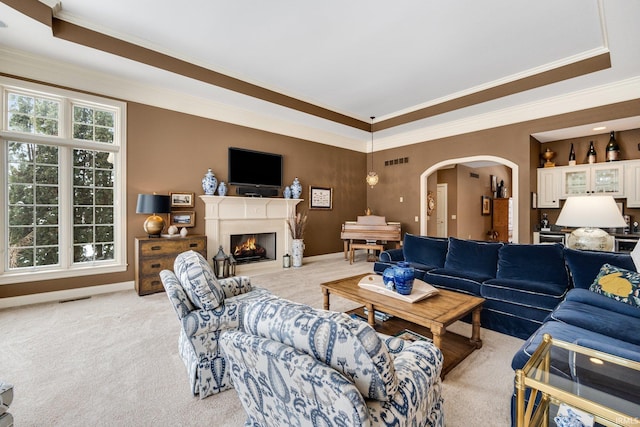 living area with arched walkways, a tray ceiling, a warm lit fireplace, and visible vents