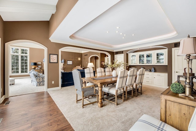 dining space featuring baseboards, visible vents, arched walkways, light wood-style flooring, and a tray ceiling