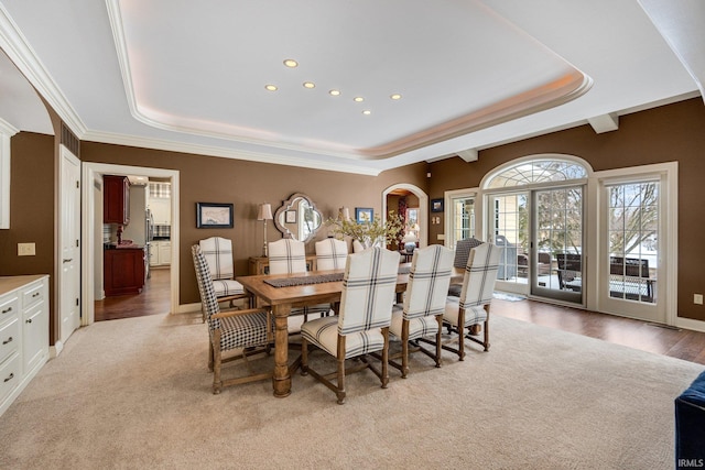 dining space featuring arched walkways, a tray ceiling, crown molding, light wood-style floors, and recessed lighting